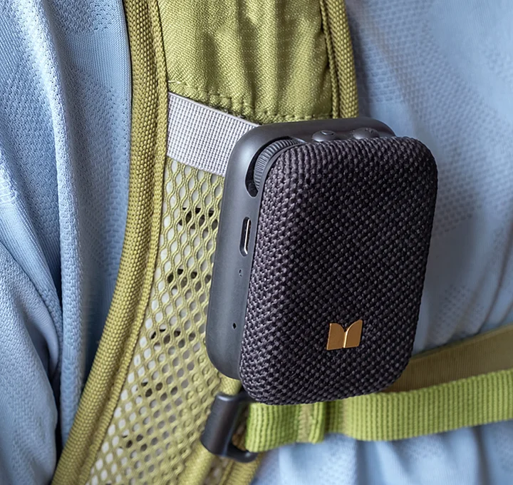 Fekete mini Bluetooth-hangszóró, amely egy hátizsák olajzöld pántjára van rögzítve